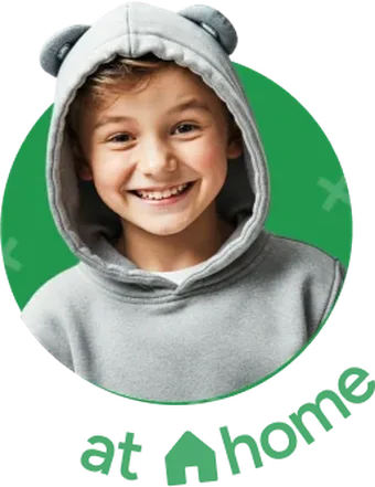 Un niño sonriente con sudadera gris con capucha, con la etiqueta «en casa» en inglés